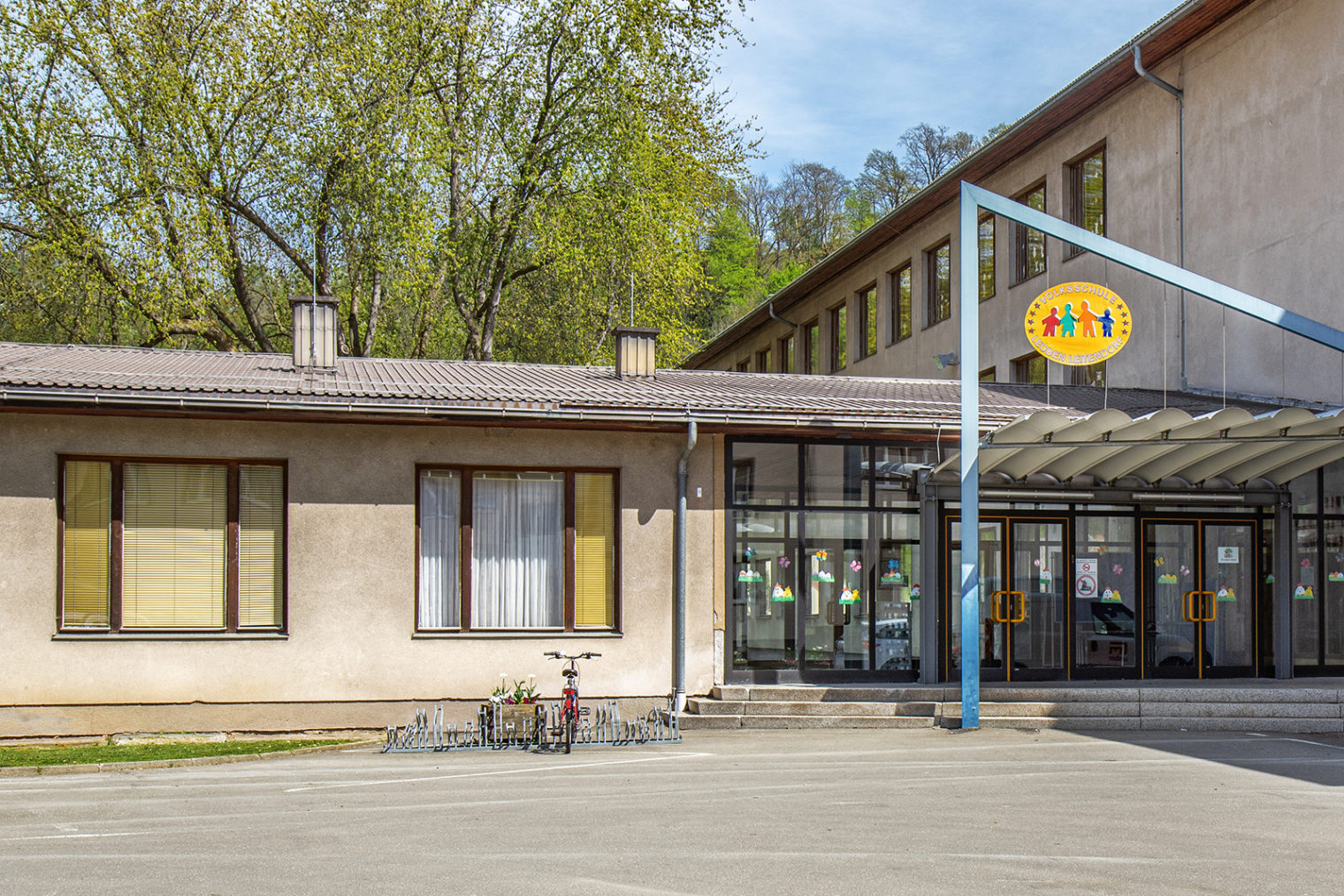 Volksschule Leoben-Leitendorf mit Fahrradständer und Logo vor dem Eingangsbereich