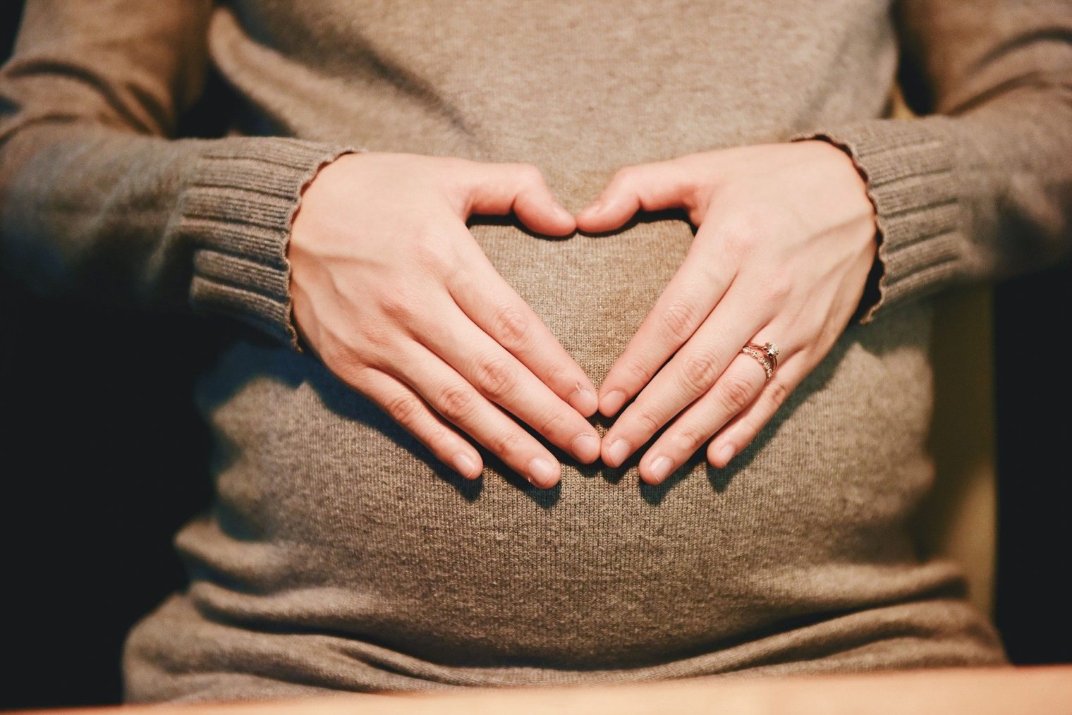 Hände bilden Herzform auf dem Schwangerschaftsbauch