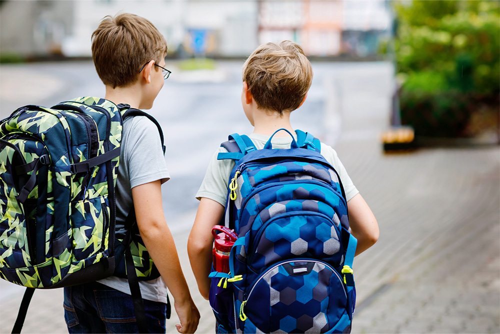 Zwei Kinder mit Schulrucksack blicken auf die Straße
