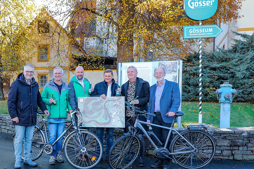 Bürgermeister und andere Repräsentanten posieren sie mit Fahrrädern vor dem Gösser und Gösseum Schild