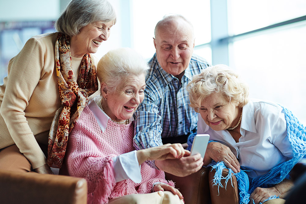 Drei ältere Damen und ein Herr beschäftigen sich mit einem Smartphone