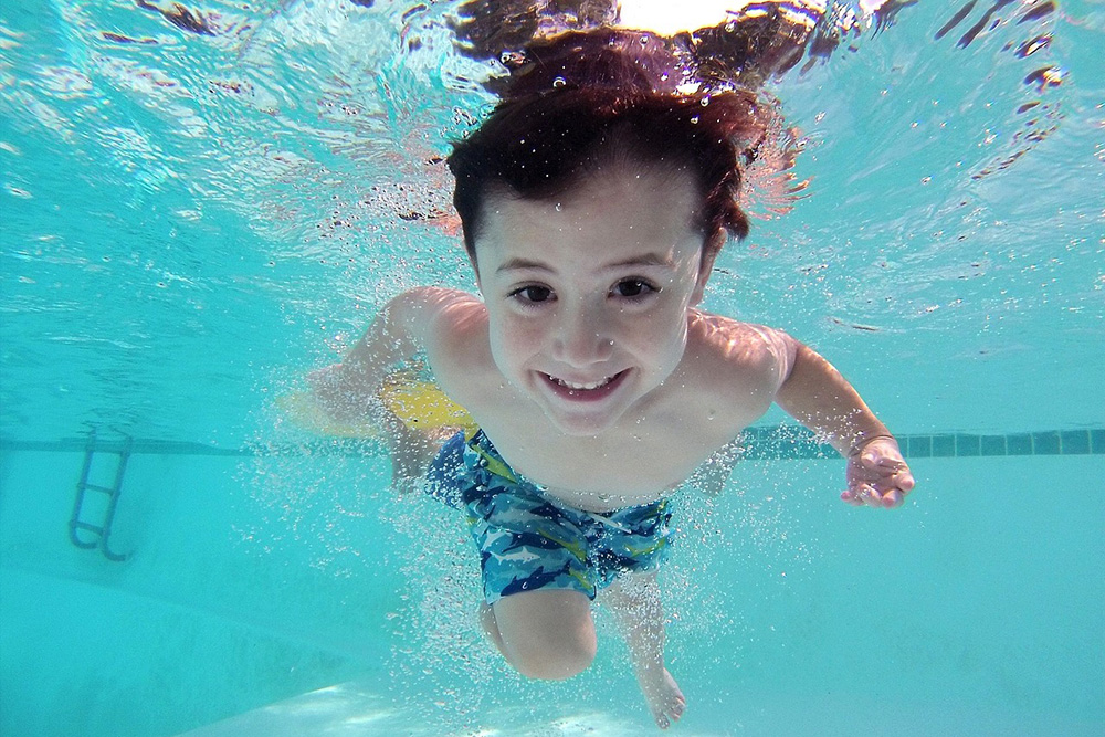 Symbolbild: Kind taucht und lächelt unter Wasser in die Kamera
