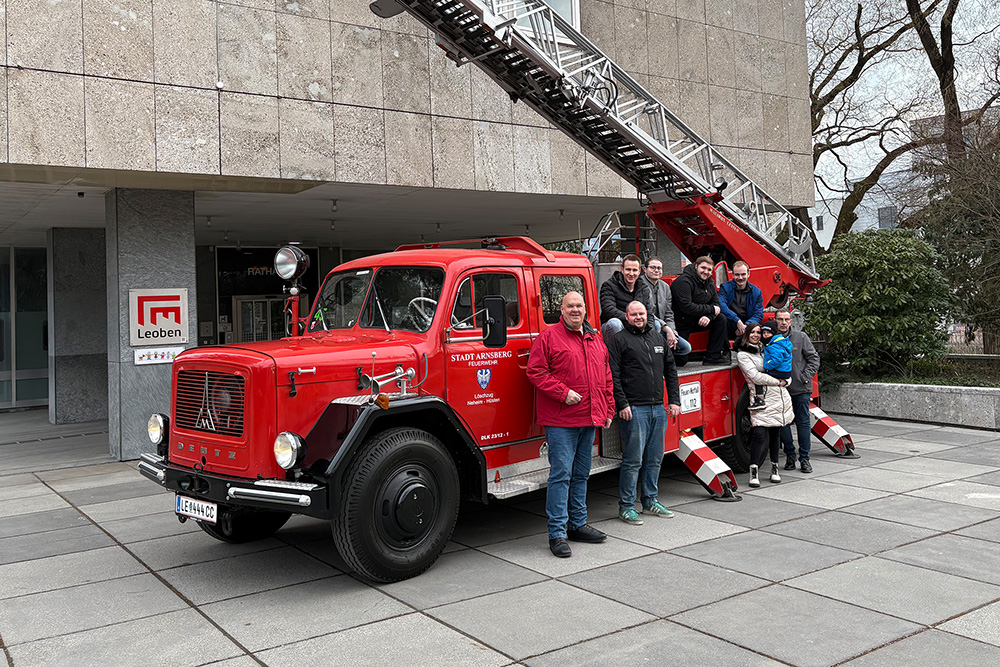 Feuerwehrauto-Oldtimer und neun Personen davor