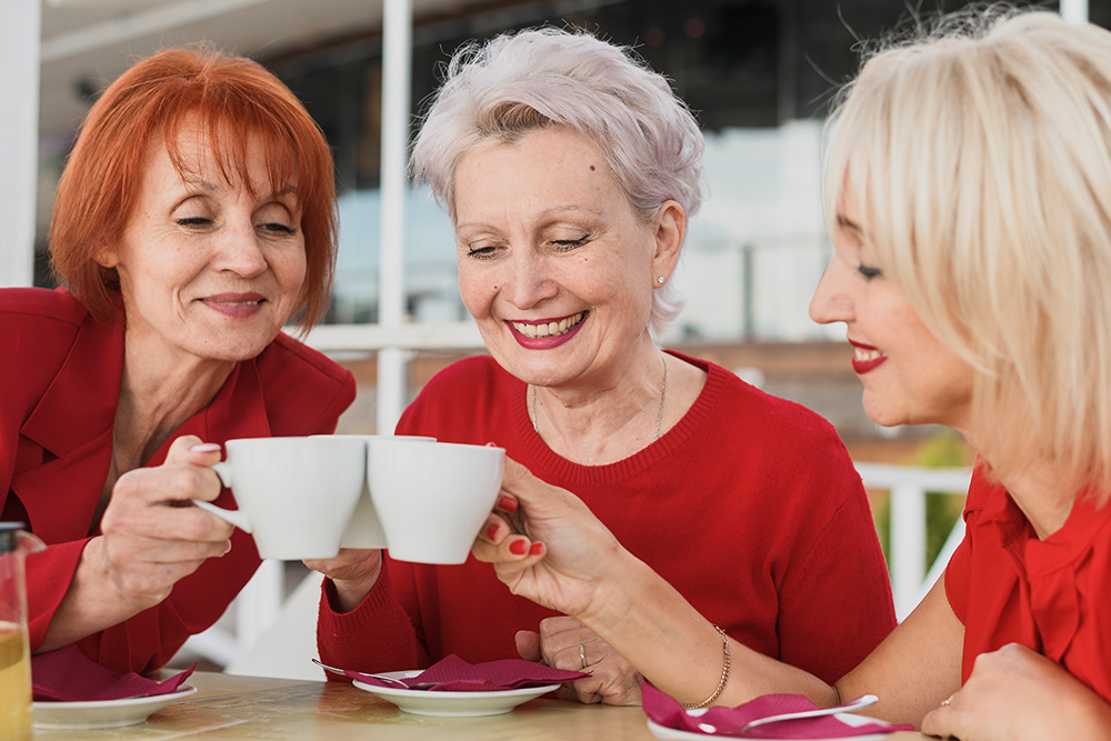Drei Seniorinnen stoßen mit Kaffeetassen an