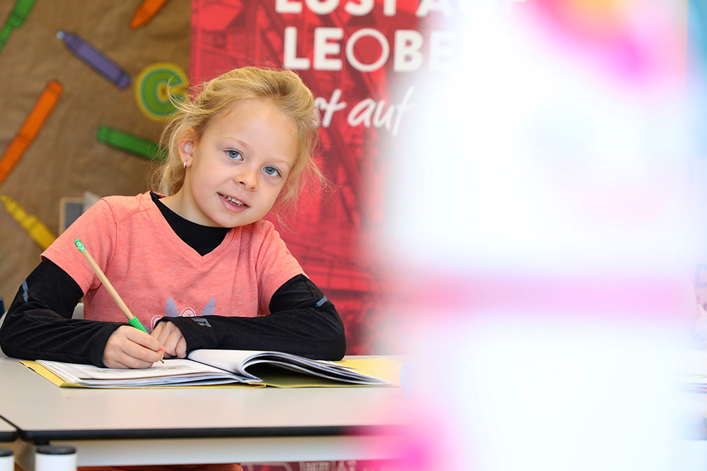 Schulkind an Tisch mit Heft und Stift