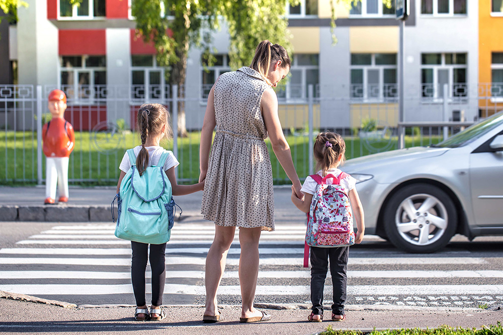 Mutter mit zwei kleinen Mädchen wartend vor Schutzweg bei vorbeifahrendem Auto