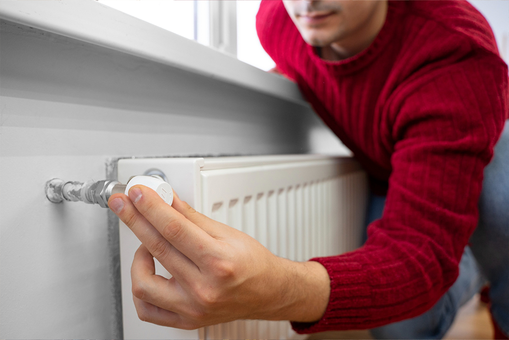 Heizkörper, bei dem ein Mann in rotem Pullover und blauer Jeans am Thermostat dreht