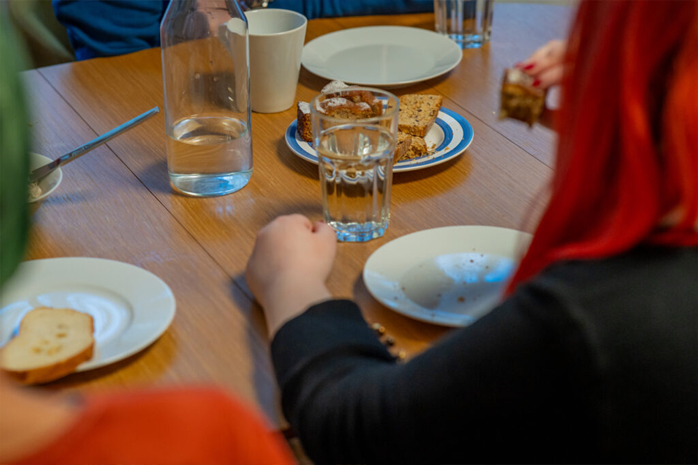 Frau mit roten Haaren sitzend bei Kuchen, Kaffee und Wasser