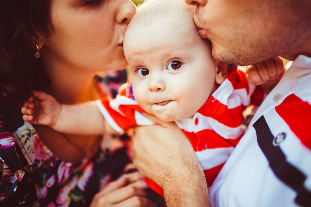 Symbolbild Eltern küssen Baby das in die Kamera schaut