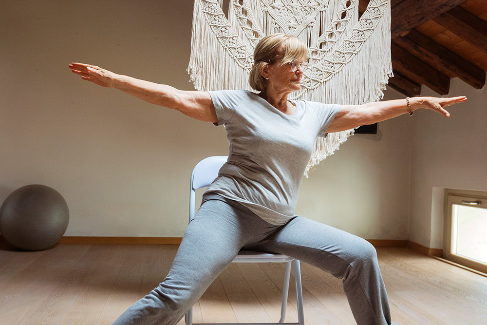 Ältere Frau macht Turnübungen am Sessel