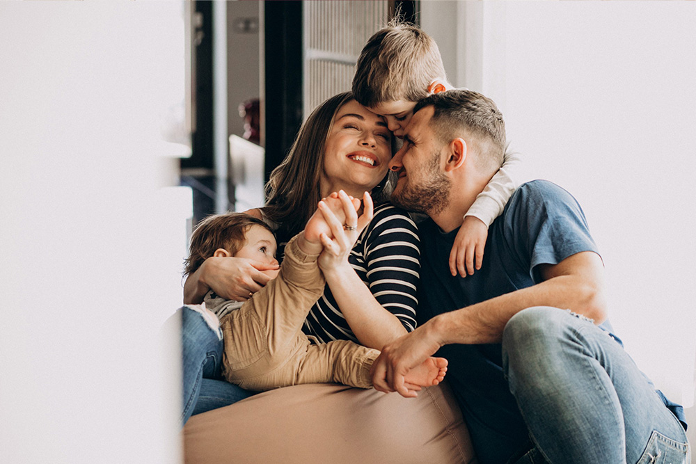 Symbolbild: Familie (Mutter und Vater mit zwei kleinen Kindern) beim Kuscheln