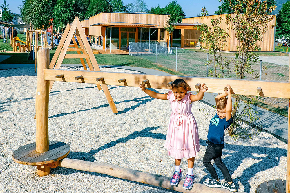 Zwei spielende Kinder (ein Mädchen und ein Bub) im Kindergarten im Außenbereich beim Balancieren auf einem Spielgerüst