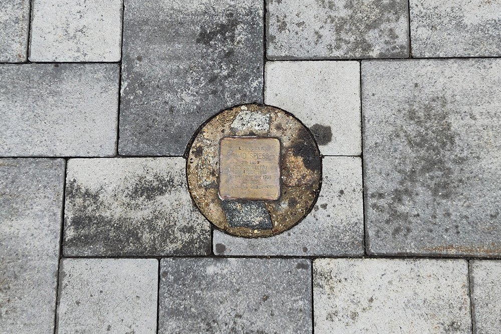Am Boden inmitten von Pflastersteinen einbetonierter Stolperstein David Spiess