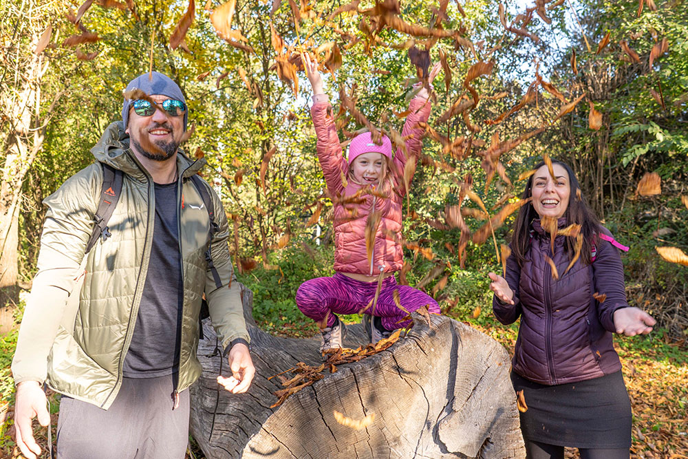 Fröhliches Familienfoto Herbst (Mutter, Vater, Kind) Mädchen wirft Laub in die Luft